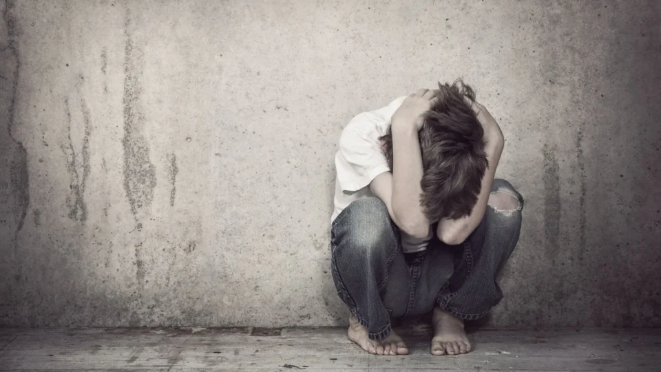 boy with his head in his hands leaning against a wall